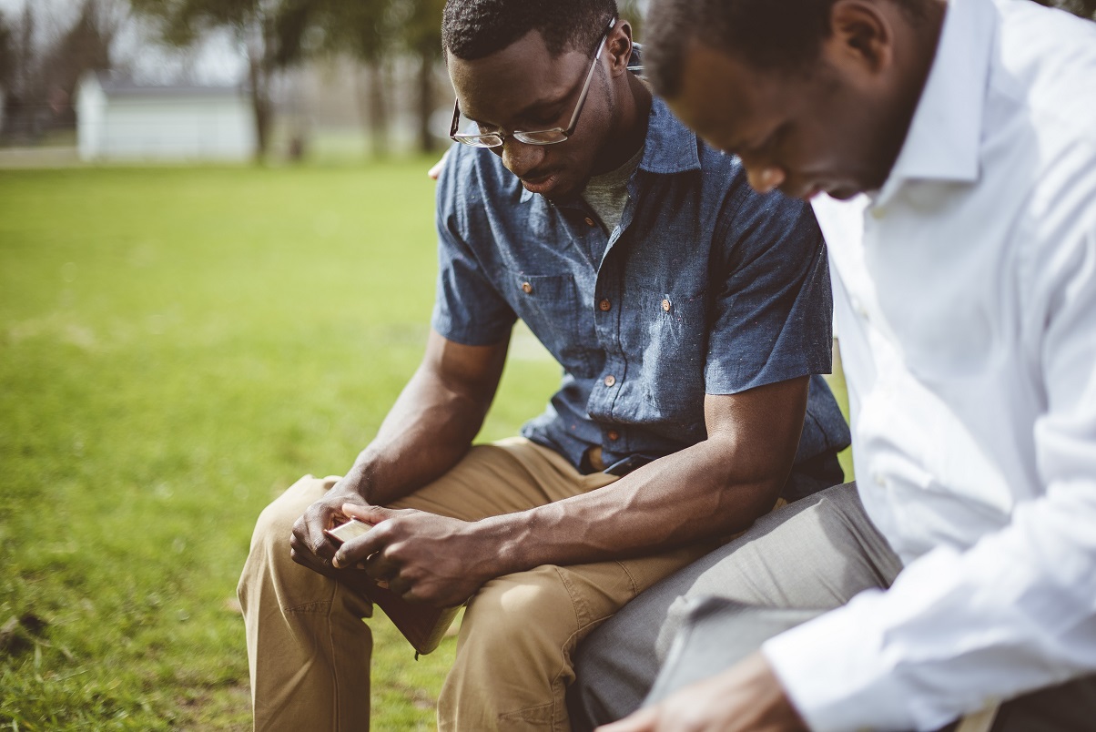Two African-American male friends sitting and praying with closed eyes and the Bible in their hands